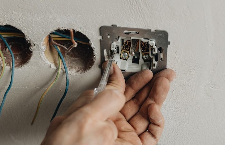 Eine Hand installiert einen elektrischen Anschluss in einer Wand mit freiliegenden Drähten.