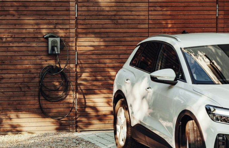 Weißes Elektroauto parkt neben einer Holzverkleidung mit einer Ladestation.