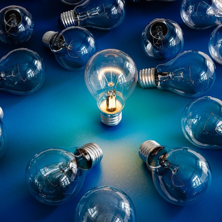 Eine einzelne Glühbirne leuchtet unter vielen unbeleuchteten Glühbirnen auf einem blauen Hintergrund.